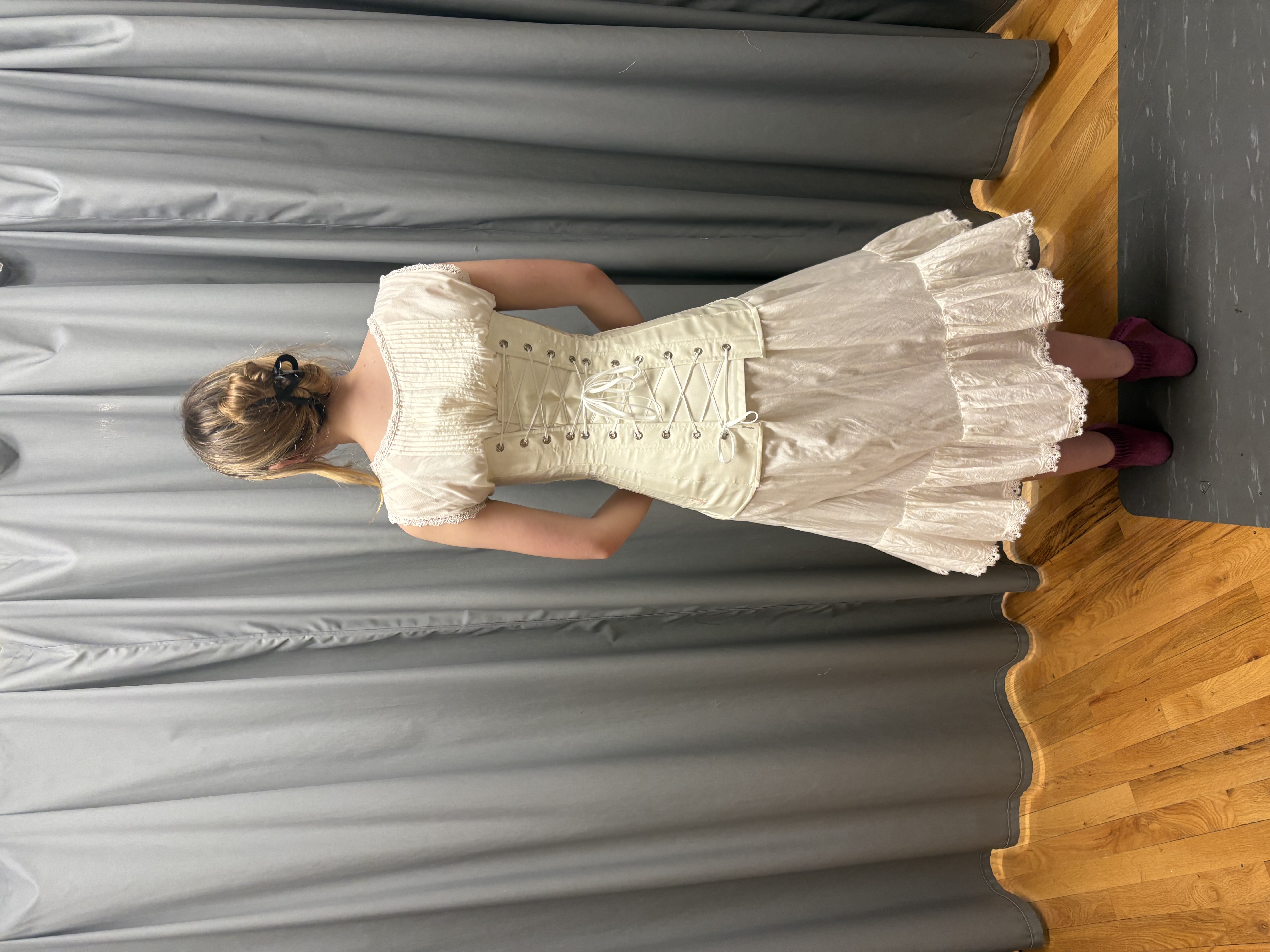 A woman in a long chemise wearing a white longline corset, full length back view