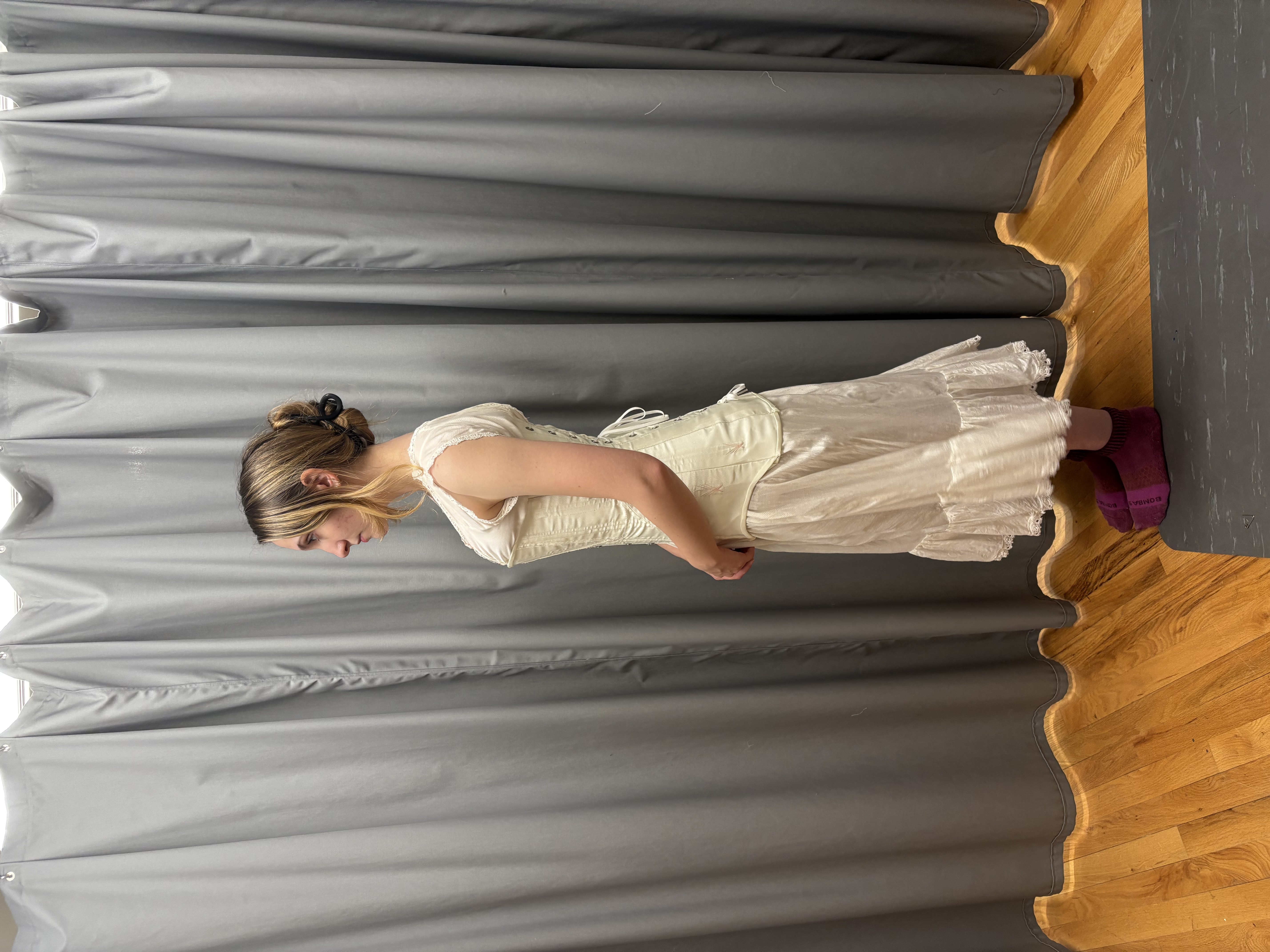 A woman in a long chemise wearing a white longline corset, full length back view