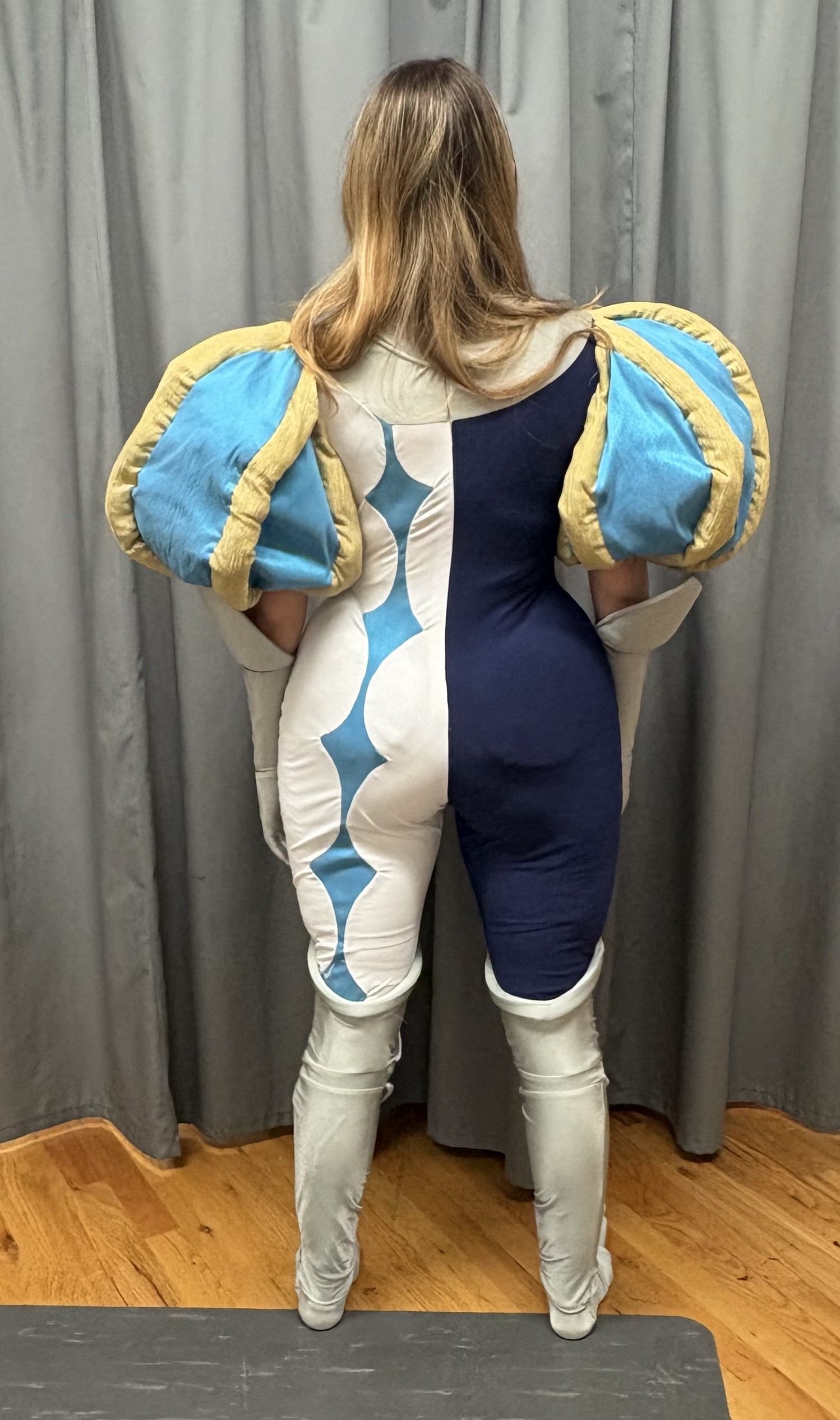 A woman in a navy, white, and blue bodysuit with big sleeves, back view