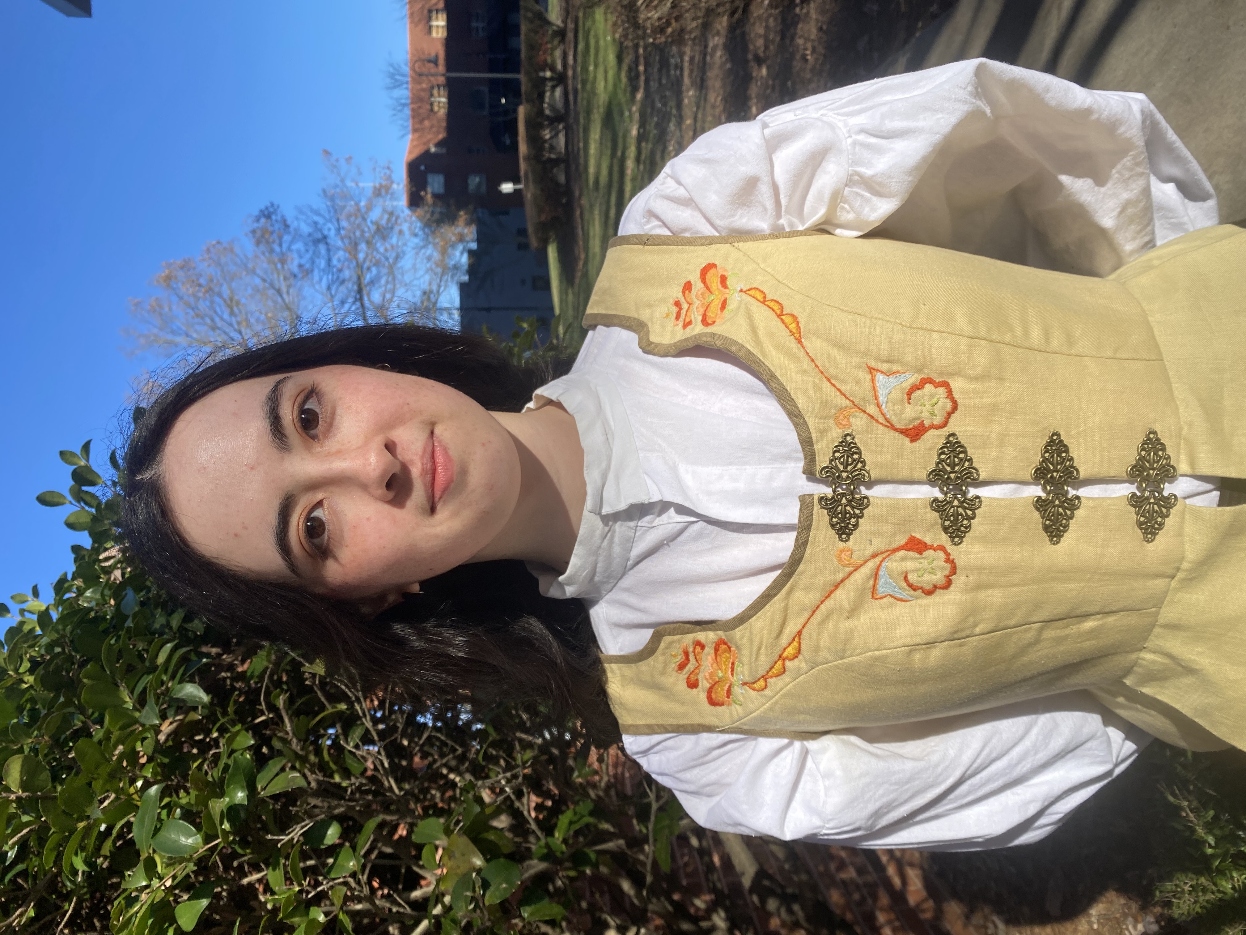 A woman in a long sleeve white shirt with a yellow bodice on top, front view