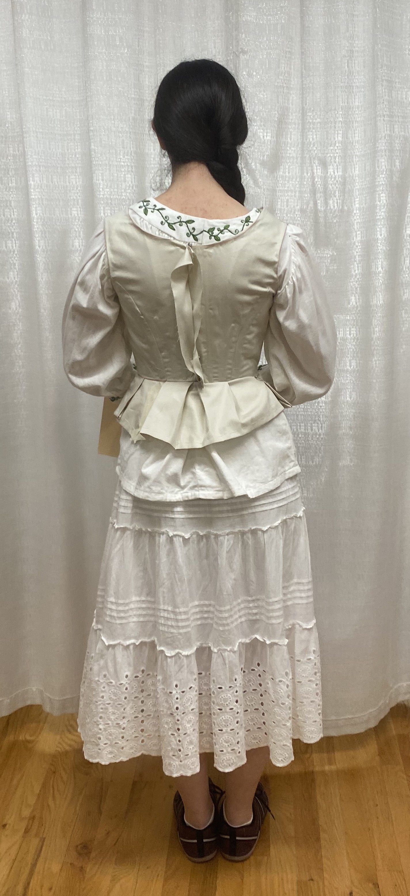 A woman in a long sleeve white shirt with a muslin bodice mock up on top, back view