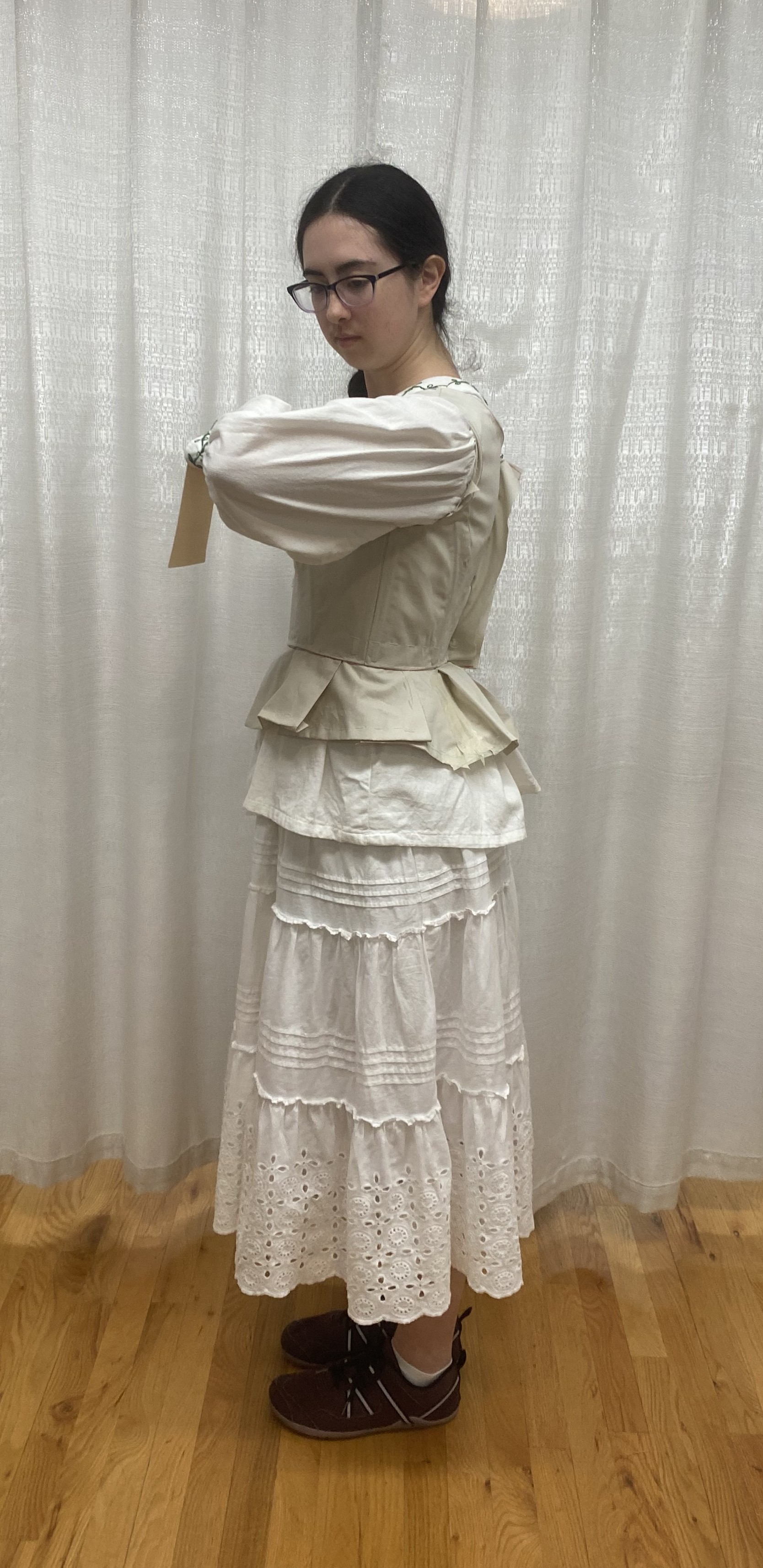 A woman in a long sleeve white shirt with a muslin bodice mock up on top, side view