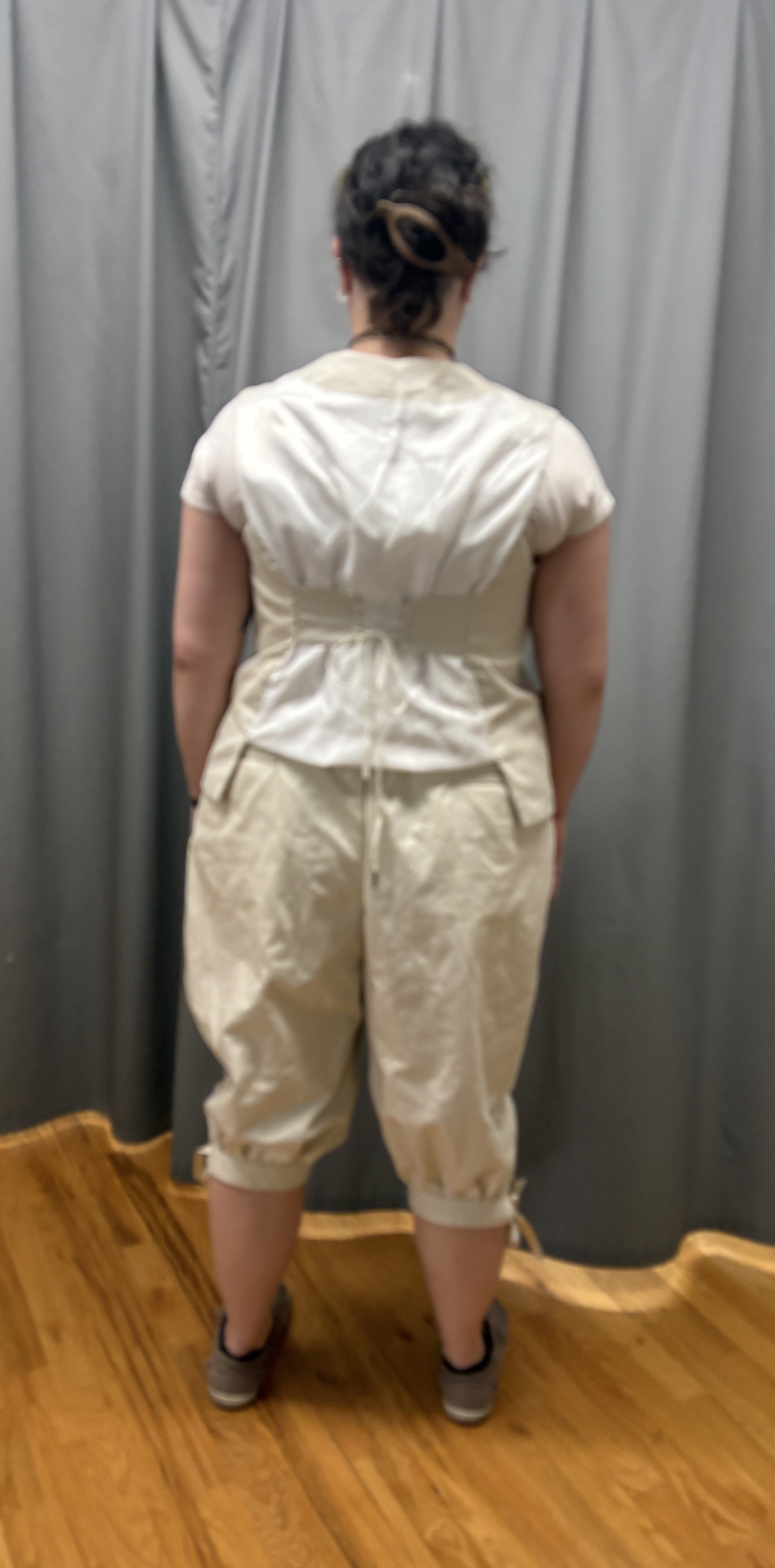 A woman in a beige georgian vest and pair of breeches, full length back view