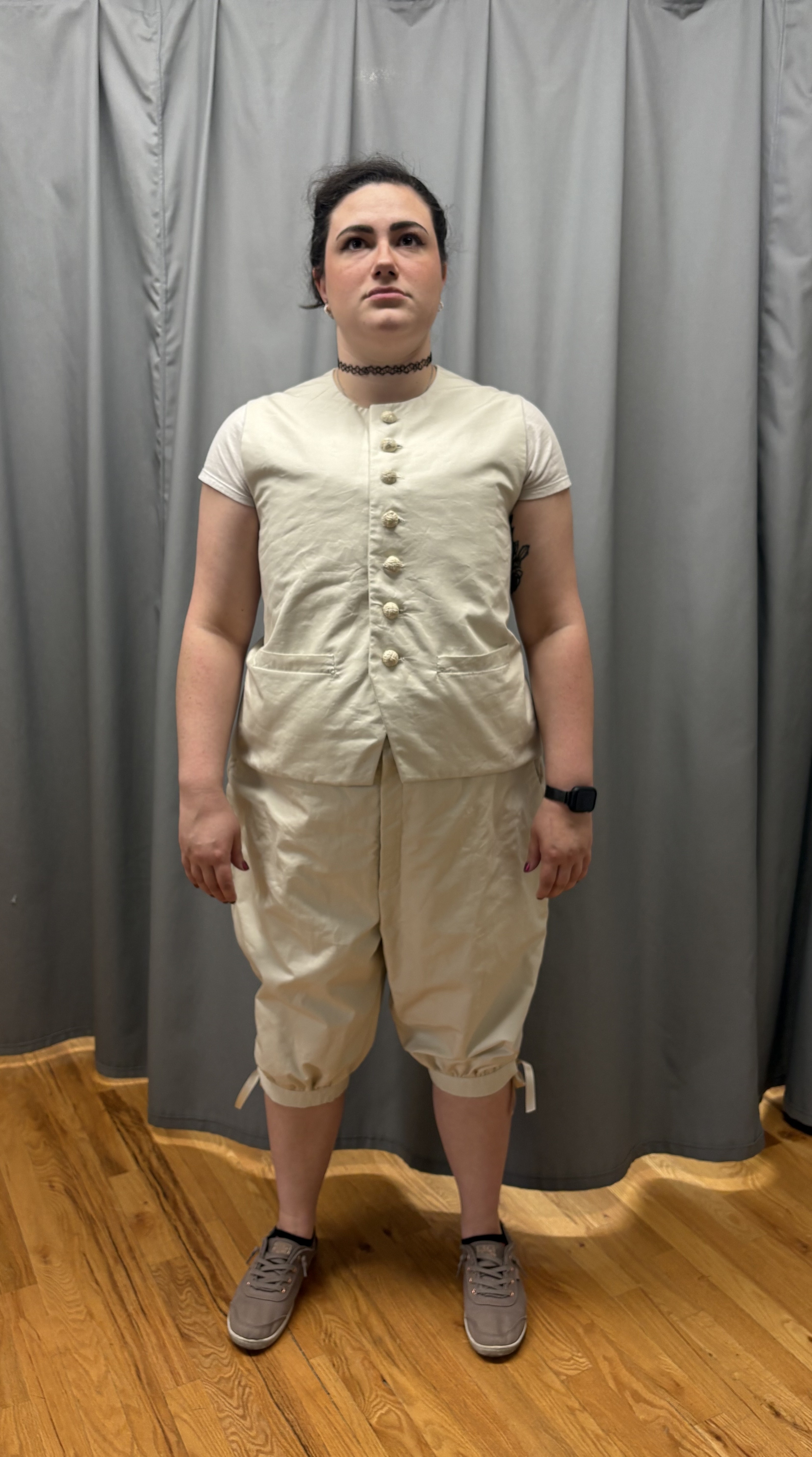 A woman in a beige georgian vest and pair of breeches, full length front view