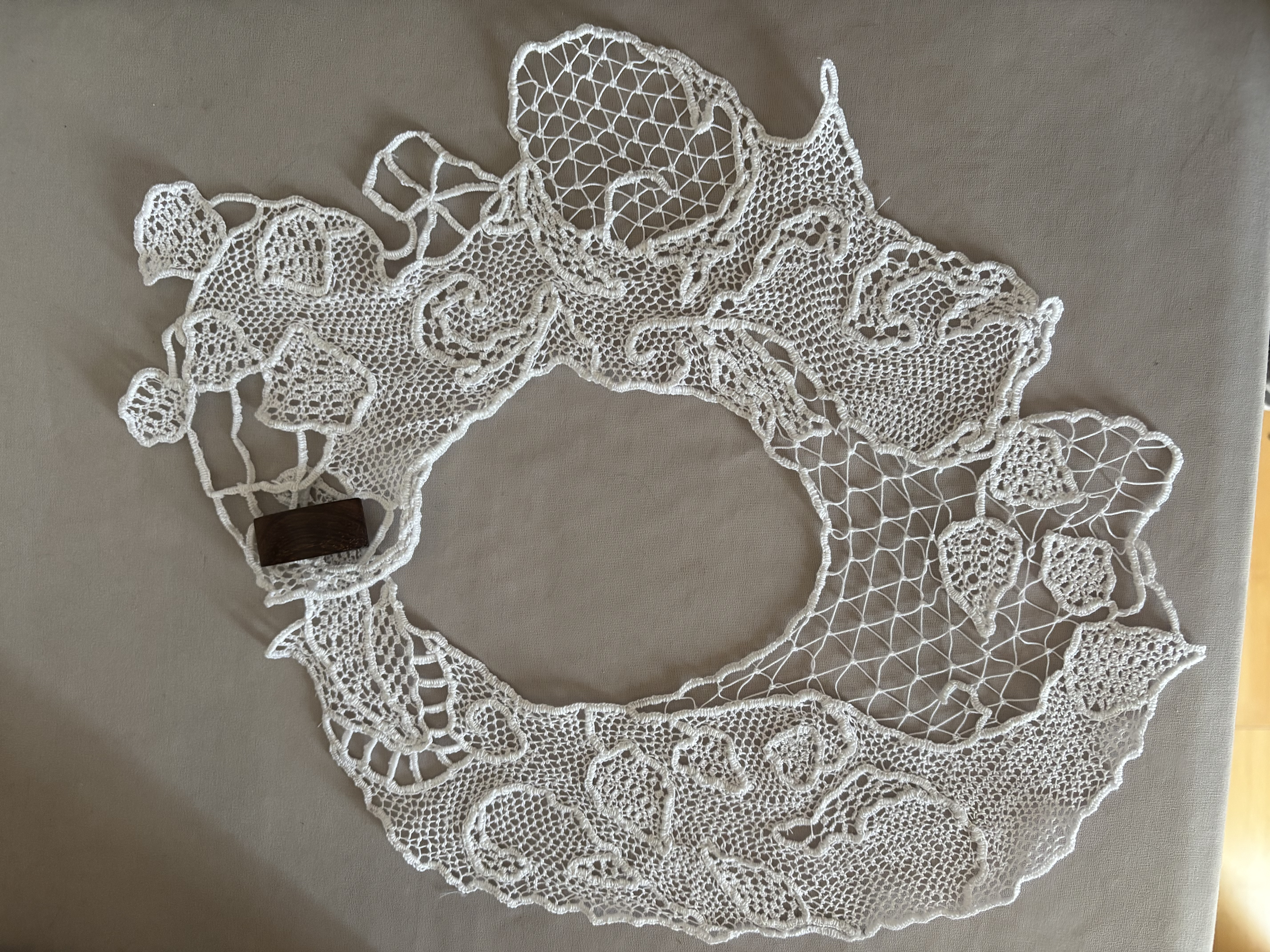 white lace collar featuring leaves and vines, closed with a wooden toggle