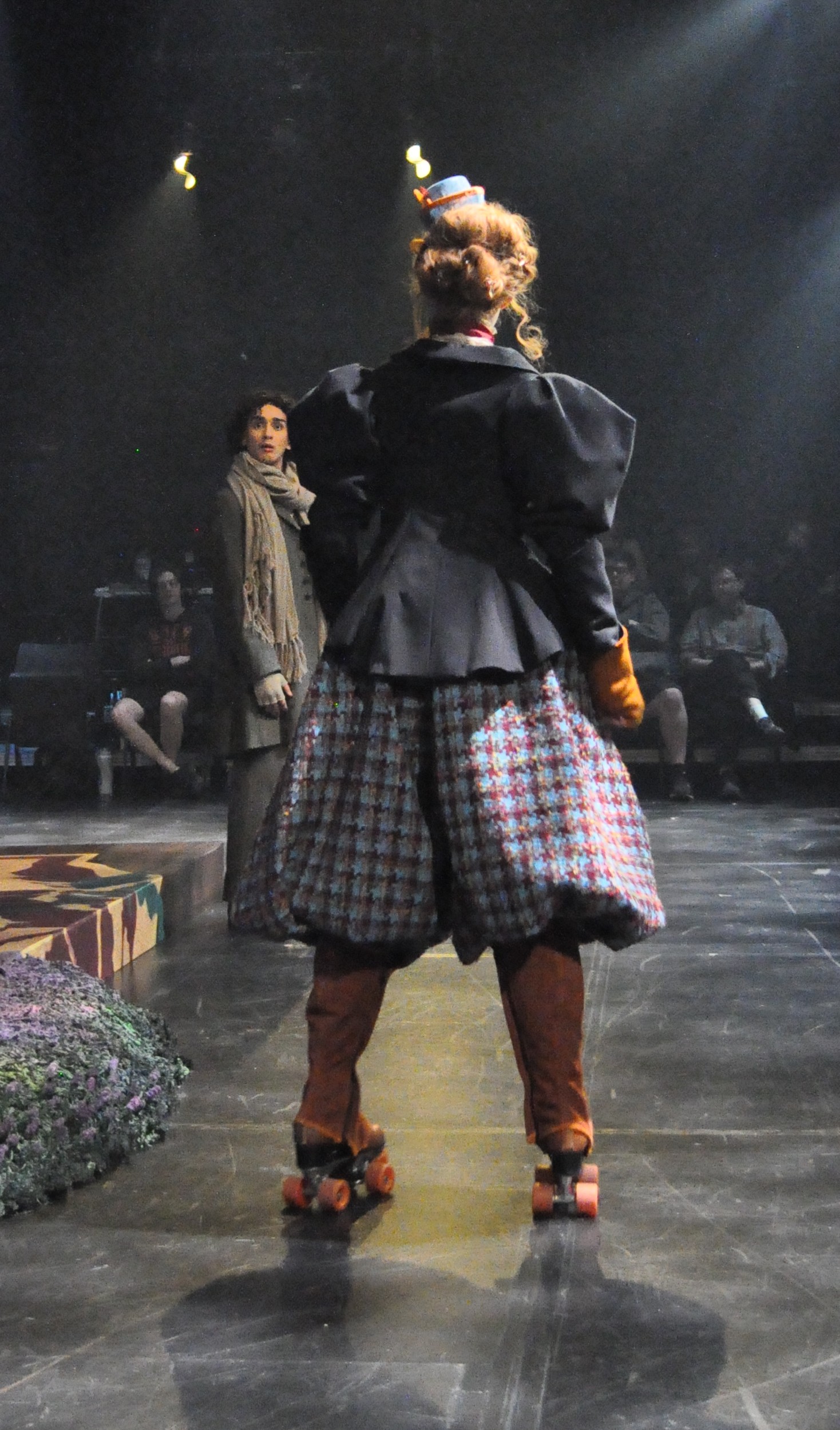 A woman on skates wearing voluminous plaid bicycle pants/breeches with a taylored vicotrian women's jacket, standing facing BACK
