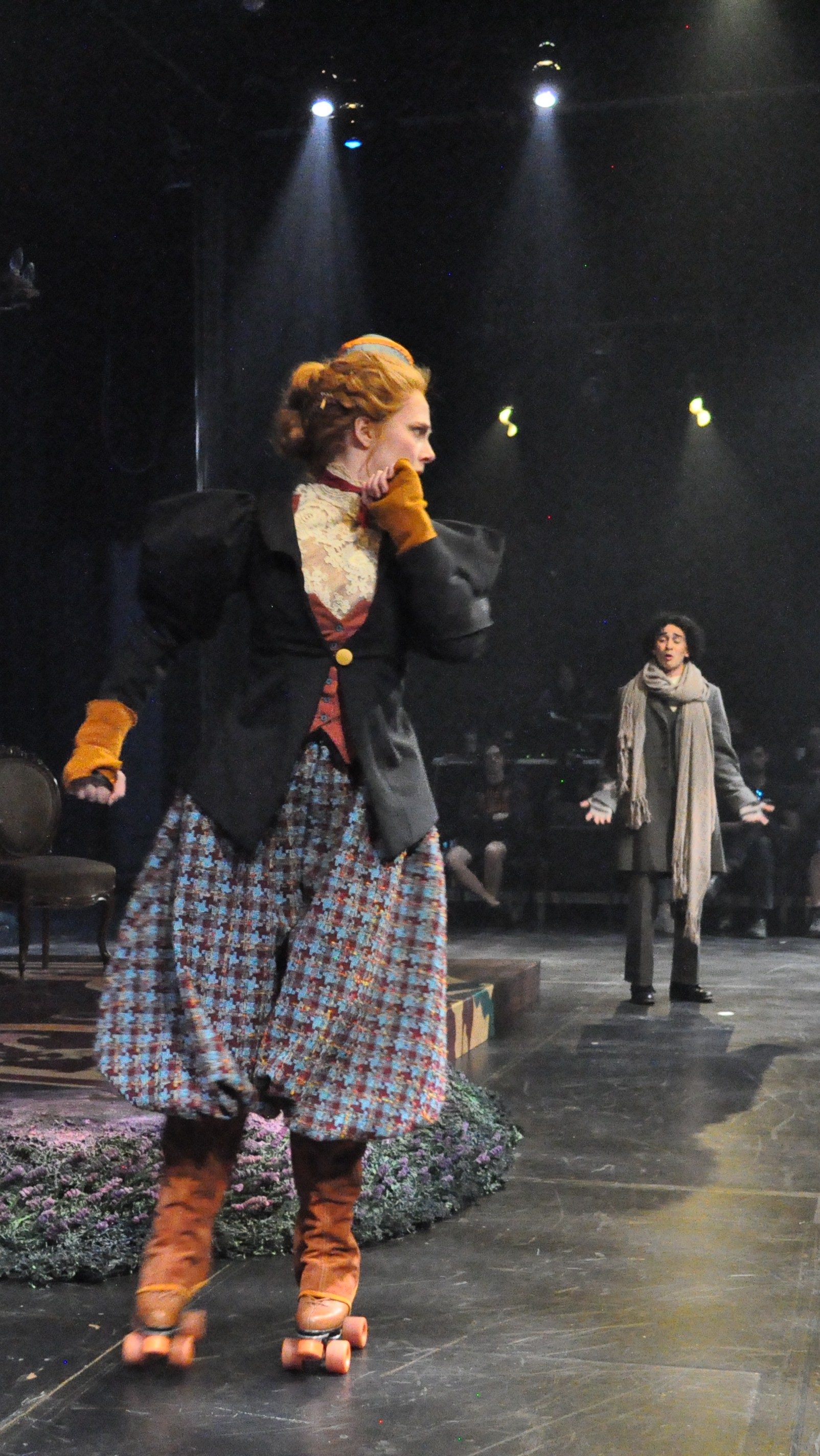 A woman on skates wearing voluminous plaid bicycle pants/breeches with a taylored vicotrian women's jacket, standing facing front
