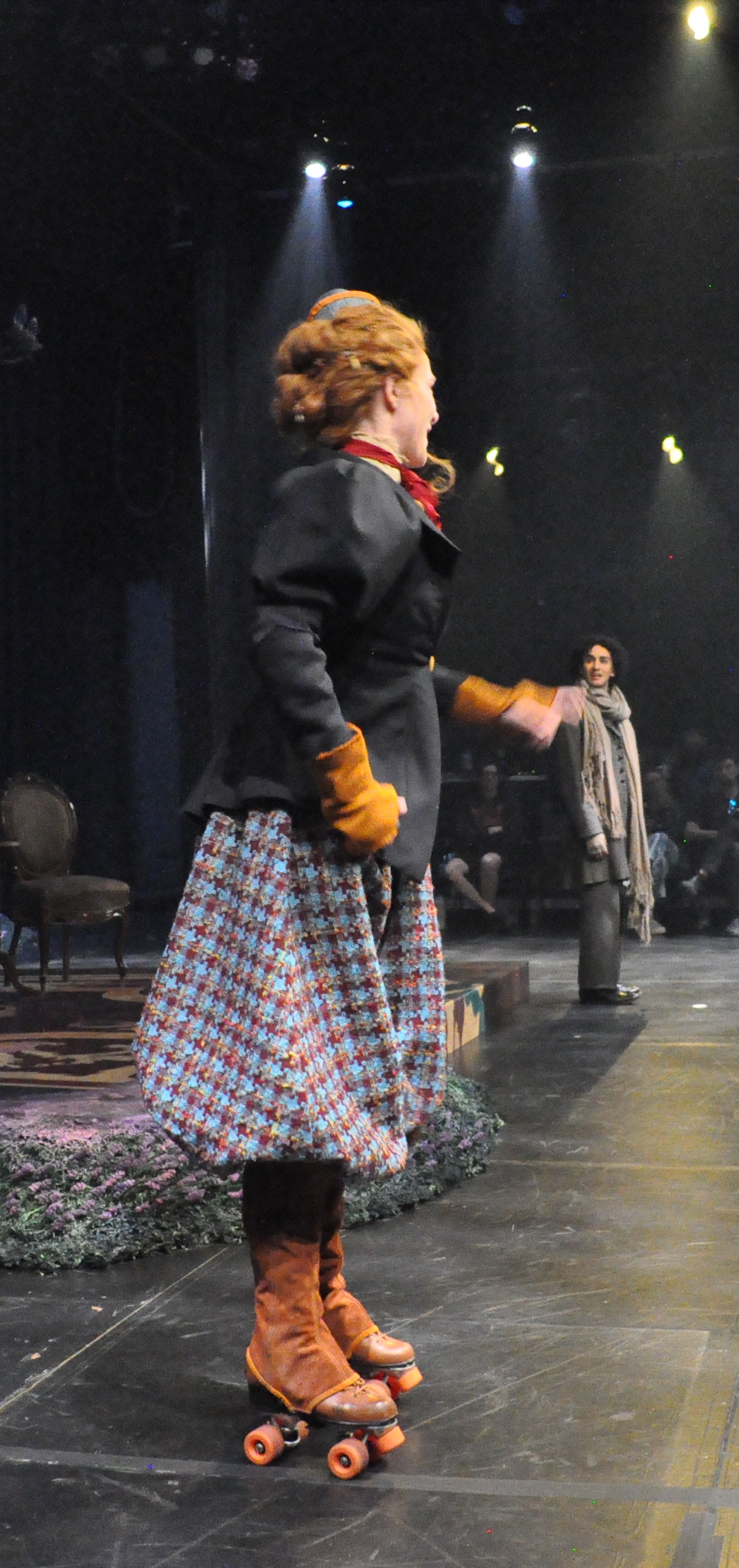 A woman on skates wearing voluminous plaid bicycle pants/breeches with a taylored vicotrian women's jacket, side view