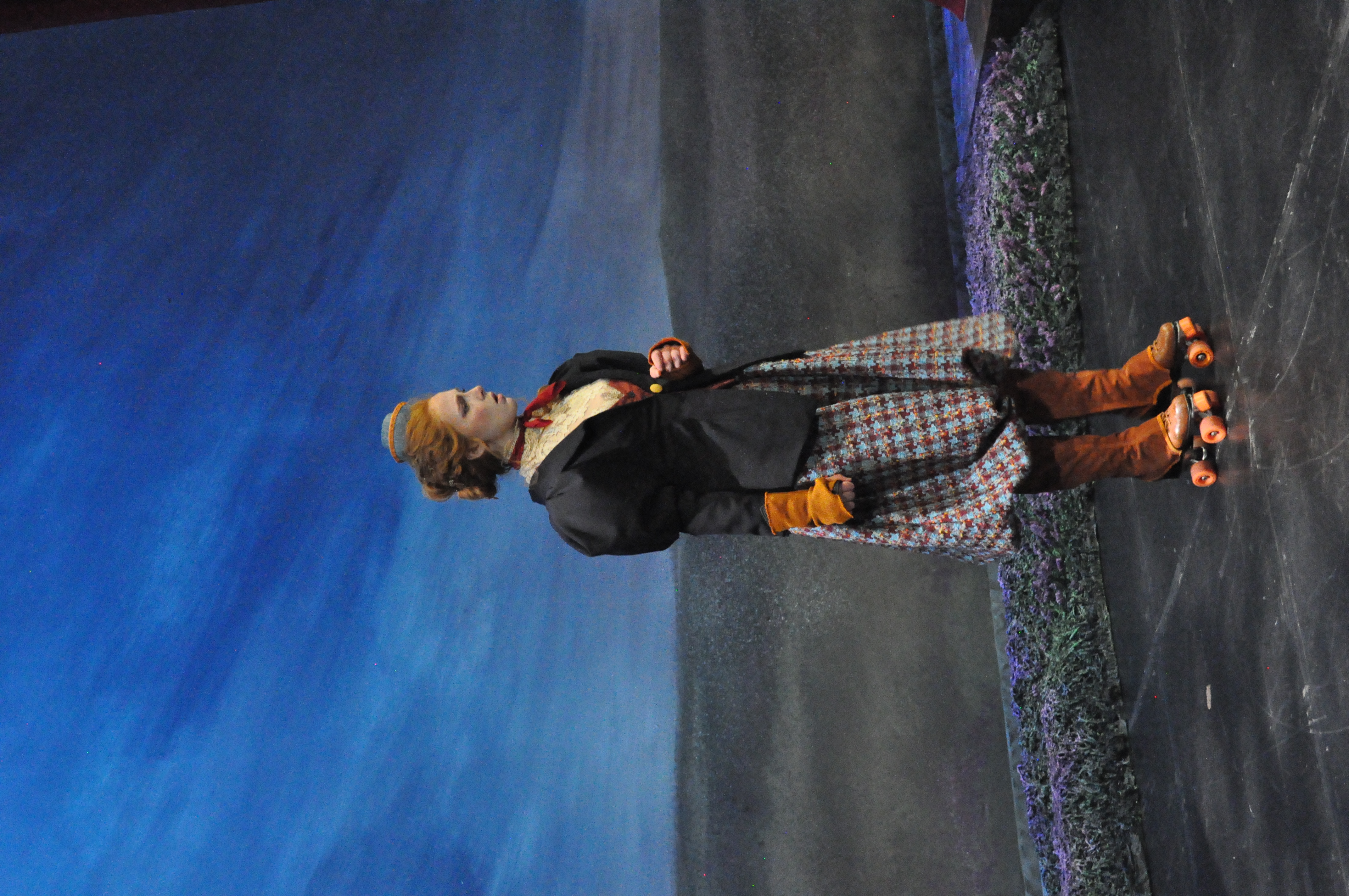 A woman on skates wearing voluminous plaid bicycle pants/breeches with a taylored vicotrian women's jacket, 3/4 view