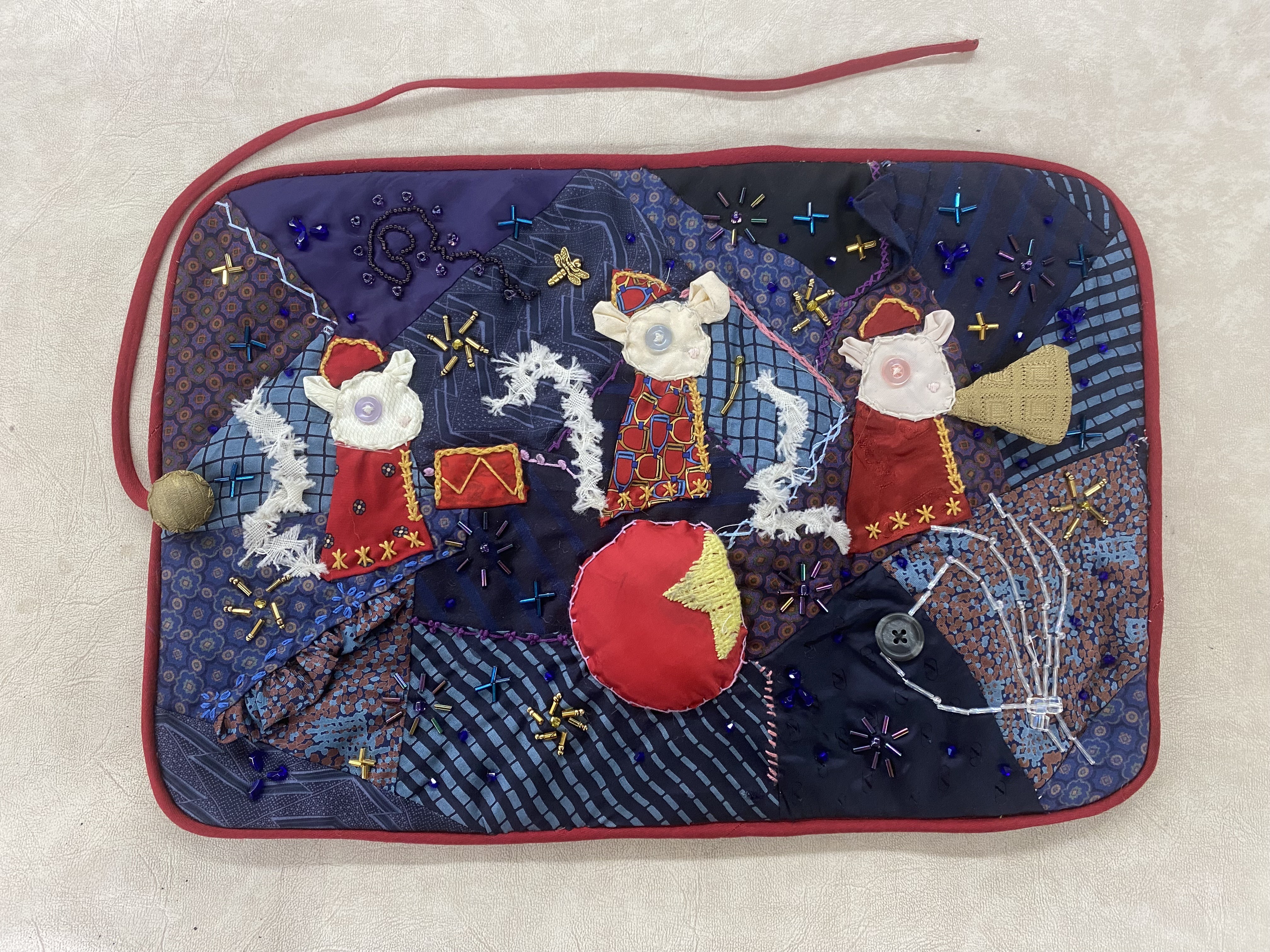 a crazy quilt with a blue and purple background featuring three mice circus members in red band uniforms.